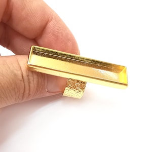 May include: Gold-toned adjustable ring with a rectangular, open-top bezel. The bezel is approximately 2.5 inches long and 0.75 inches wide.