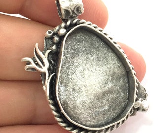 May include: Silver pendant with a rope-like border and a large oval-shaped opening for a stone or other embellishment. The pendant has a detailed floral design on one side and a loop for attaching a chain on the top.