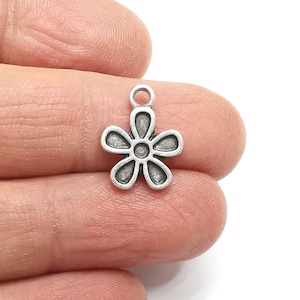 Pode incluir: Encanto de prata em forma de flor com cinco pétalos. A flor tem um pequeno círculo no centro.