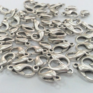 May include: A pile of silver-toned metal lobster claw clasps, commonly used for jewelry making.