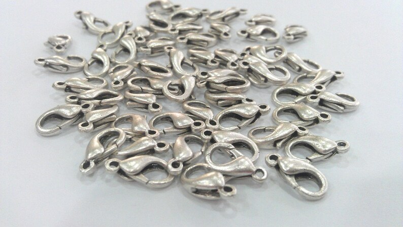May include: A pile of silver-toned metal lobster claw clasps, commonly used for jewelry making.