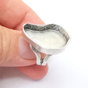 Puede incluir: Un anillo de plata con un engaste grande de forma ovalada. El engaste es liso y tiene un borde ligeramente elevado.