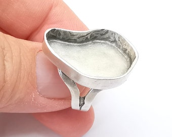 May include: A silver ring with a large, oval-shaped setting. The setting is smooth and has a slightly raised edge.