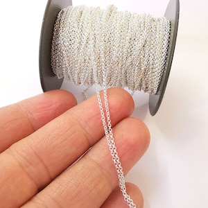 May include: A spool of silver chain, with a length of chain extending from the spool. The chain is a fine, delicate chain.