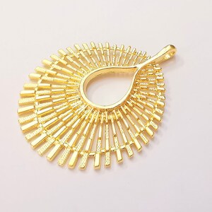 May include: Gold-toned metal pendant with a sunburst design. The pendant has a teardrop-shaped opening in the center.
