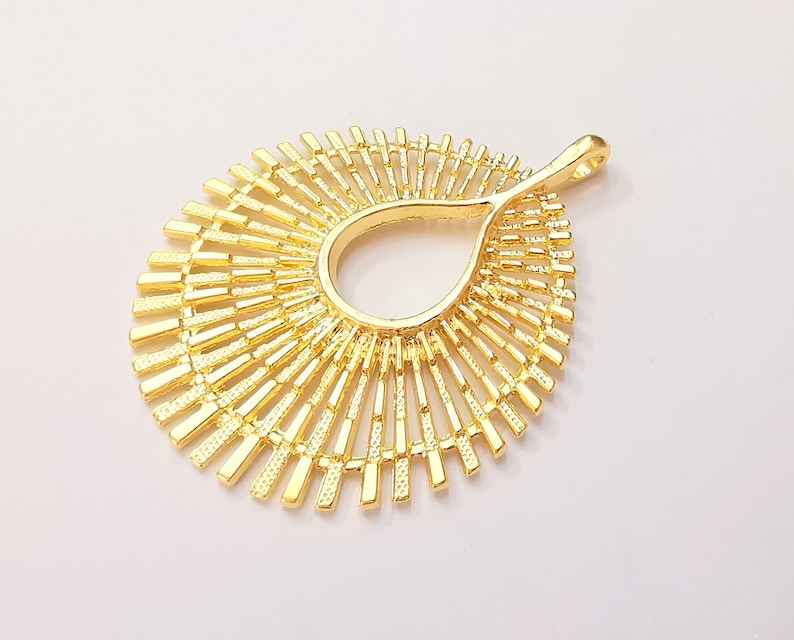 May include: Gold-toned metal pendant with a sunburst design. The pendant has a teardrop-shaped opening in the center.