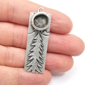 Puede incluir: Pendiente de plata con un diseño de árbol y un bisel redondo para una piedra de cabujón. El pendiente es rectangular y tiene una superficie texturizada.
