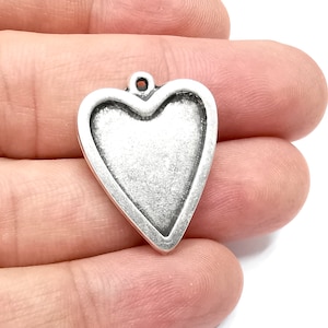 May include: A silver heart-shaped charm with a smooth, slightly textured surface. The charm has a loop at the top for attaching to a necklace or bracelet.