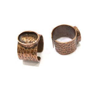 May include: Two copper ring blanks with a hammered texture. The ring blanks have a round, oval-shaped bezel for setting a cabochon stone.
