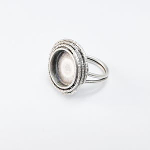 Pode incluir: Um anel de prata com uma configuração de engaste redonda e texturizada. O engaste é projetado para segurar uma pedra cabochão.