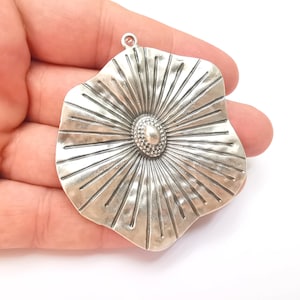 May include: Silver pendant shaped like a flower with a textured surface and a raised centre. The pendant has a loop at the top for attaching a chain.