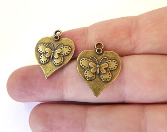 May include: Two antique gold-tone heart-shaped charms with a butterfly design. Each charm has a loop at the top for attaching to a necklace or bracelet.