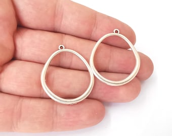 May include: Two silver oval-shaped pendant charms with a smooth, slightly textured surface. The charms have a small loop at the top for attaching to a chain or cord.