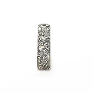 Pu&ograve; includere: Un ciondolo d'argento con un intricato design floreale. Il ciondolo &egrave; rettangolare e presenta un motivo floreale in rilievo.