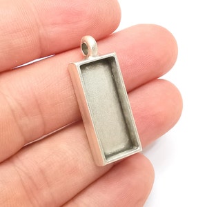 Peut inclure: Pendentif argenté avec un cadre rectangulaire ouvert pour ajouter une résine ou autre embellissement.