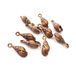 Op de afbeelding: Tien koperkleurige schelpbedels met een lus om op te hangen. De bedels zijn gedetailleerd met een textuur die lijkt op een schelp.