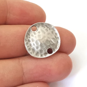 Puede incluir: Encanto de metal plateado con textura martillada y dos agujeros. El encanto es redondo y tiene una forma ligeramente irregular.