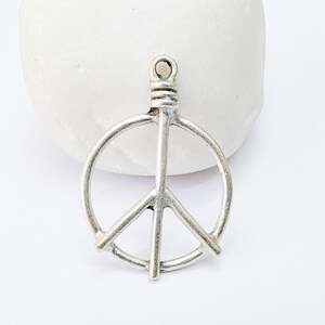 May include: Silver peace sign charm pendant with a loop at the top for attaching to a necklace or bracelet.