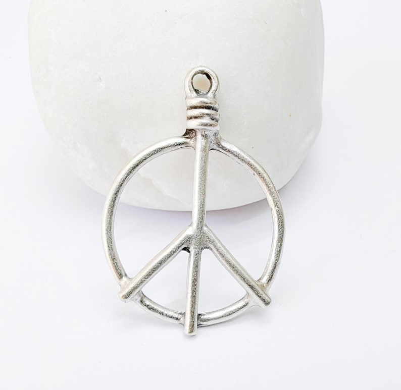 May include: Silver peace sign charm pendant with a loop at the top for attaching to a necklace or bracelet.