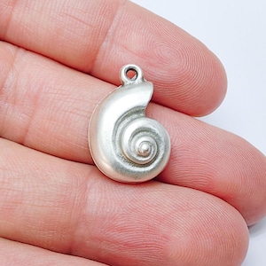Peut inclure: Un charm en forme de coquillage de couleur argentée avec un motif en spirale. Le charm possède une petite boucle en haut pour l'attacher à un collier ou un bracelet. Le charm mesure environ 2 cm de long.