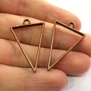 May include: Two copper triangle shaped pendant frames with a loop at the top for hanging.