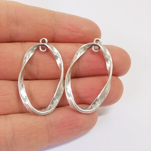 May include: Two silver oval-shaped pendant charms with a twisted design. The charms have a loop at the top for attaching to a necklace or bracelet.