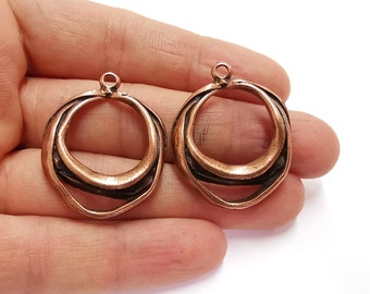 May include: Two copper-colored metal rings with a textured, wavy design. The rings have a small loop at the top for attaching to a chain or other jewelry.