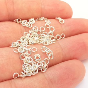 Könnte beinhalten: Ein Haufen silberner Sprungringe, eine Art Schmuckzubehör, in einer Hand. Die Ringe sind klein und rund und eignen sich perfekt zum Verbinden verschiedener Schmuckstücke.