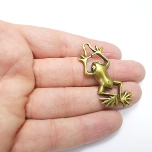 May include: A gold-toned metal frog charm with a detailed design. The frog is in a climbing pose with its legs outstretched.