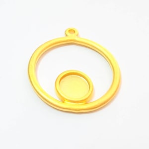 May include: Gold-toned metal pendant with a round frame and a smaller round cutout in the center. The pendant has a loop at the top for attaching a chain.