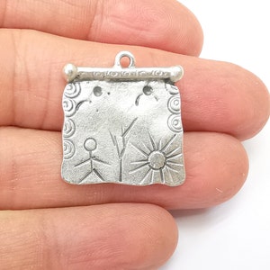 Puede incluir: Colgante de plata con un diseño de estilo dibujado a mano de una figura de palo, un árbol y un sol. El colgante está unido a una barra de plata con un bucle en la parte superior.