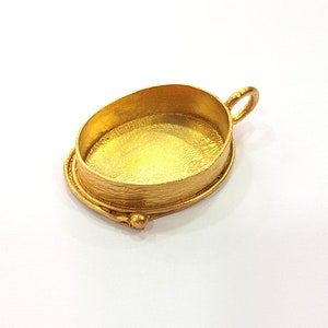 Puede incluir: Engaste de colgante ovalado en tono dorado con una superficie lisa y texturizada y un bucle para sujetar una cadena. El engaste está diseñado para sujetar una piedra cabujón.