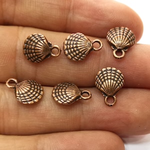 May include: A set of eight copper-colored metal shell charms with a loop for attaching to jewelry or crafts.