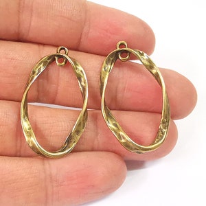 Peut inclure: Deux breloques ovales en métal doré avec un design torsadé. Chaque breloque a une petite boucle en haut pour l'attacher à des bijoux.