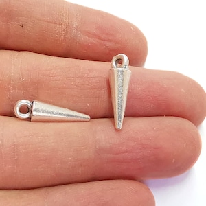 Może przedstawiać: Dwa srebrne, stożkowe zawieszki z pętelką na górze. Zawieszki leżą na dłoni.