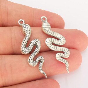May include: Two silver snake charms with detailed scales. The charms are in the shape of a snake curled up with its tail in its mouth.