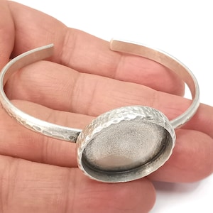Könnte beinhalten: Silberarmband mit einer runden, gehämmerten Metallfassung für einen 25 mm Cabochon. Das Armband ist offen und verstellbar.