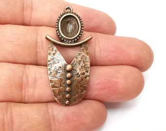 May include: A copper-toned pendant with a textured, oval-shaped design. The pendant features a round, open space in the center, perfect for adding a gemstone or other embellishment. The pendant has a hammered metal look and a decorative, geometric design.