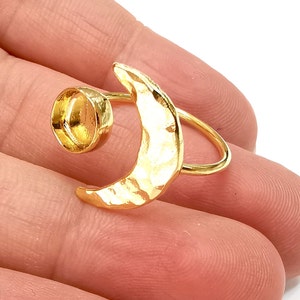 May include: Gold ring featuring a hammered crescent moon design and a round bezel setting. The ring is open and adjustable.