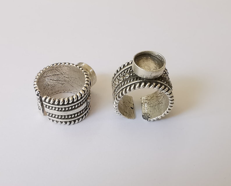 Puede incluir: Dos anillos de plata con un dise&ntilde;o decorativo. Un anillo tiene un engaste redondo y vac&iacute;o para una piedra o cabuj&oacute;n.