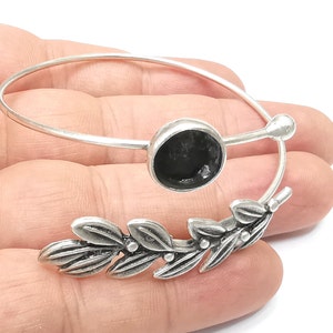 May include: Silver bangle bracelet with a black cabochon and a leaf design.