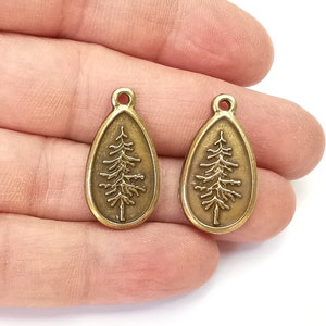 May include: Two antique gold-toned metal charms shaped like teardrops with a pine tree design.