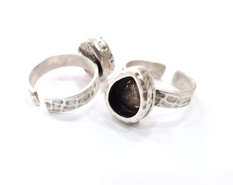 May include: Two silver rings with a textured finish. One ring has a round bezel setting, while the other has a triangular bezel setting.