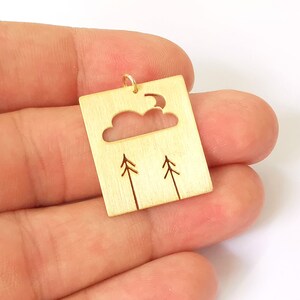 Puede incluir: Colgante de metal dorado con un diseño recortado de una nube, una luna y dos árboles.