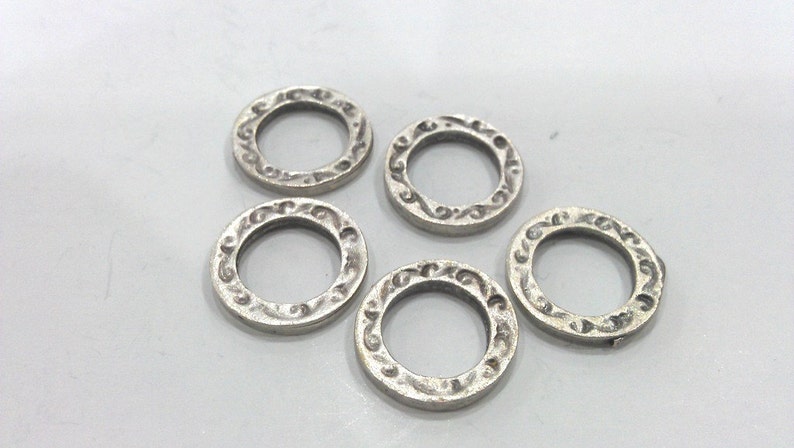 May include: Five silver-toned metal rings with an ornate design. The rings are all the same size and have a smooth, polished finish.