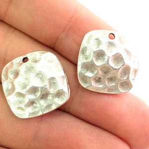 May include: Two silver square-shaped metal charms with a hammered texture and a small hole at the top for hanging.