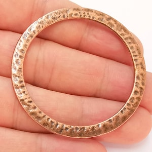 Op de afbeelding: Een koperkleurige, gehamerde metalen ring. De ring is cirkelvormig met een textuur. Het metaal heeft een warme, roodbruine tint en de gehamerde textuur voegt visuele interesse toe. Deze ring kan worden gebruikt voor het maken van sieraden of andere knutselprojecten.