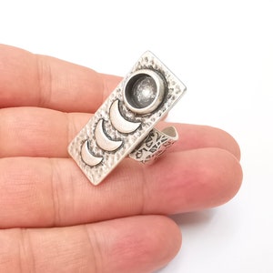 May include: Silver adjustable ring with a rectangular design featuring four crescent moons and a round bezel. The ring is textured and has a hammered finish.