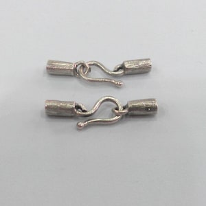 May include: Two silver-toned metal clasps with a hook and loop design. Each clasp has a cylindrical barrel with a textured surface.