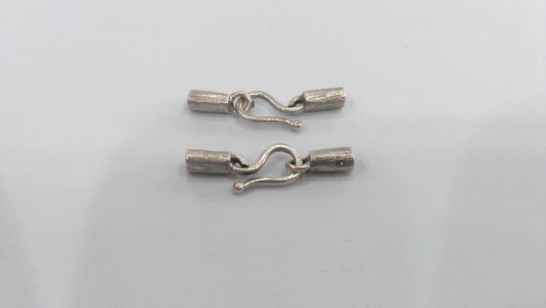 May include: Two silver-toned metal clasps with a hook and loop design. Each clasp has a cylindrical barrel with a textured surface.